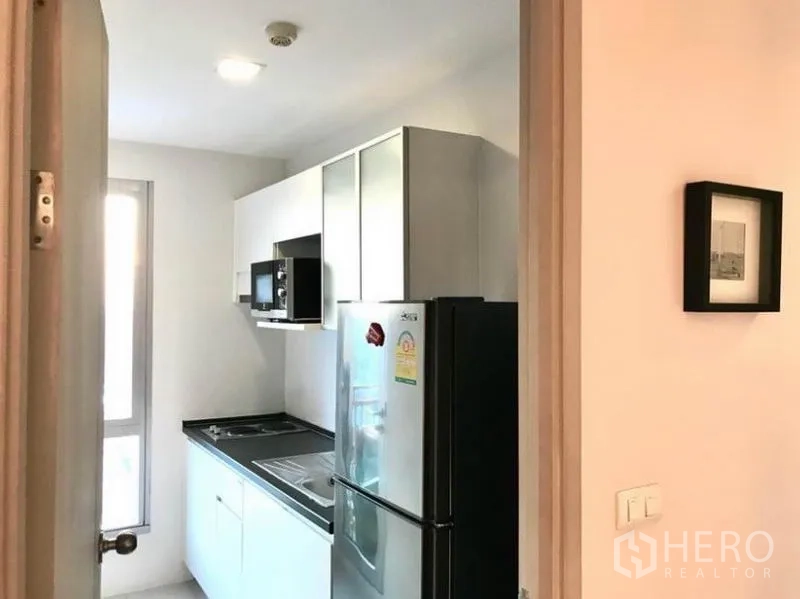 Condominium for rent in Huai Khwang, Bangkok - Compact separate kitchen with window, cabinets, cooktop, microwave and fridge.