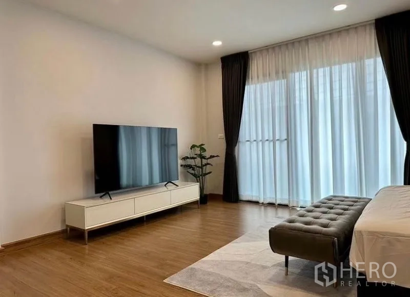 บ้าน ให้เช่าในBang Phli, Samut Prakan - ห้องนอนใหญ่พร้อมชั้นวางทีวี ม้านั่ง และผ้าม่านโปร่งสูงจรดเพดานเปิดสู่ระเบียง