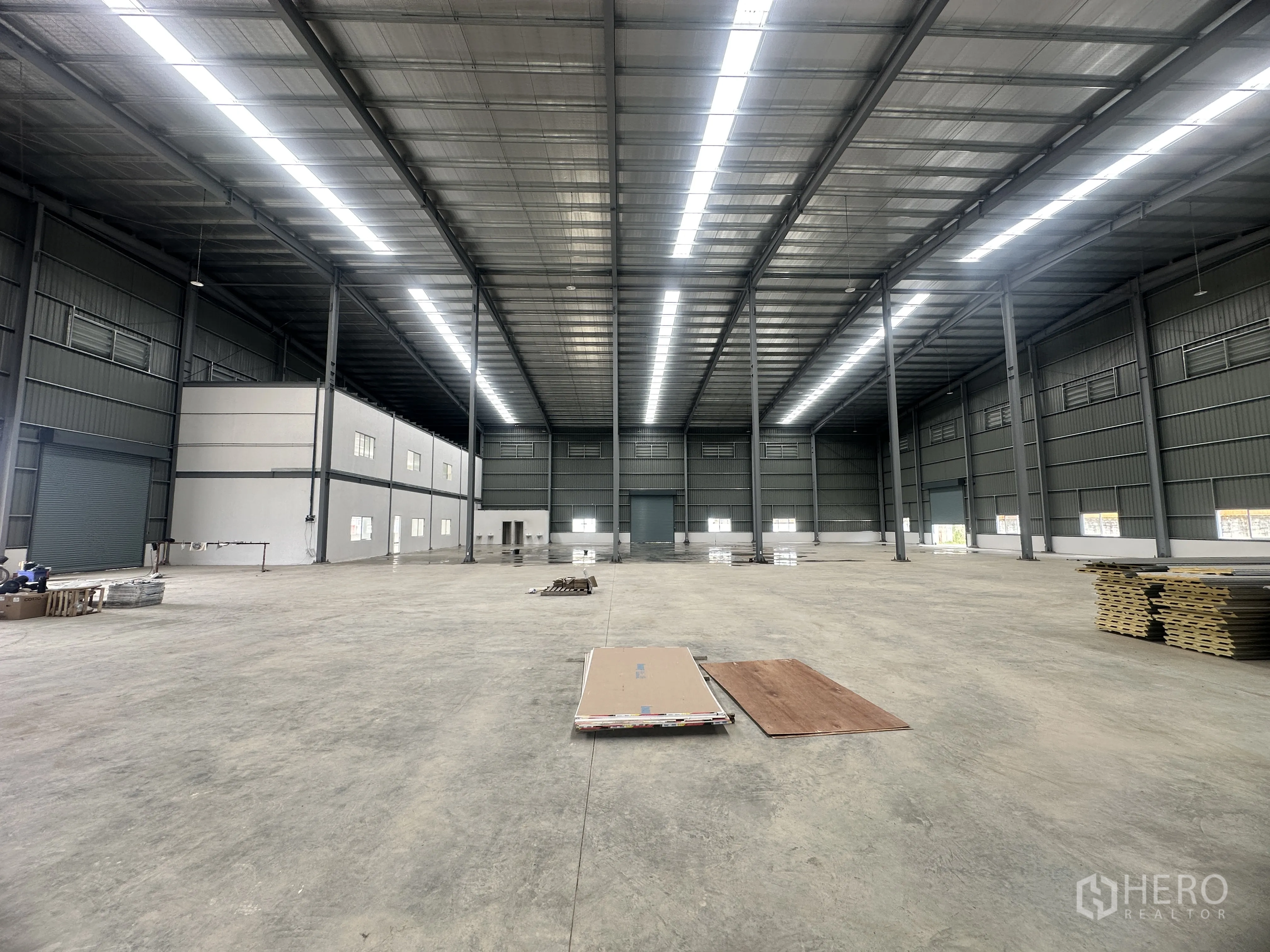 Warehouse for rent or sale in Lam Luk Ka, Pathum Thani - Interior panorama featuring a two-story office block and long roof skylights.