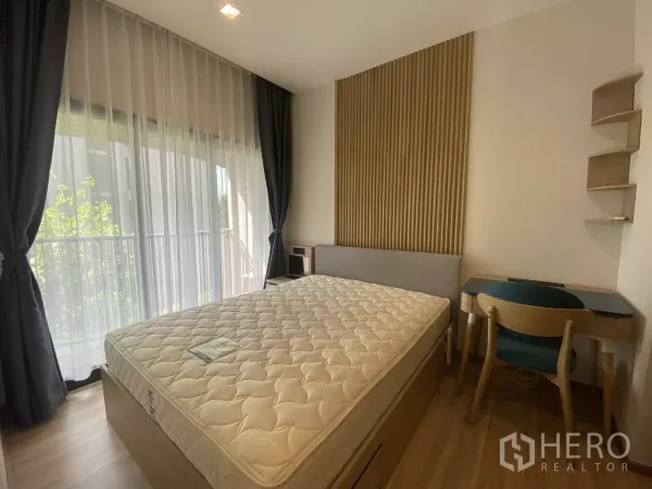 Condominium for rent or sale in Watthana, Bangkok - Cozy bedroom with large window, blackout drapes, padded headboard and a compact work desk.
