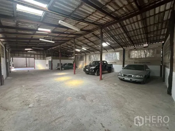 Warehouse for rent in Suan Luang, Bangkok - Wide-span storage hall with skylights, red steel columns and cars positioned near the walls.