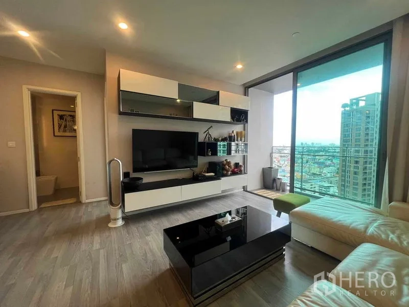 Condominium for rent in Khlong Toei, Bangkok - TV wall unit opposite sectional sofa with large balcony doors and skyline views.