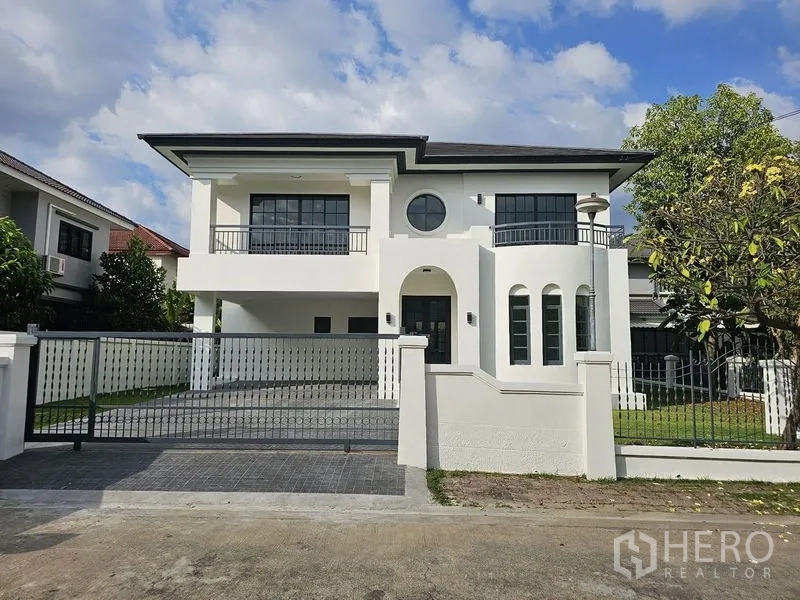 Detached House for sale in Thanyaburi, Pathum Thani - Front elevation of a gated two-storey home with driveway and lawn.