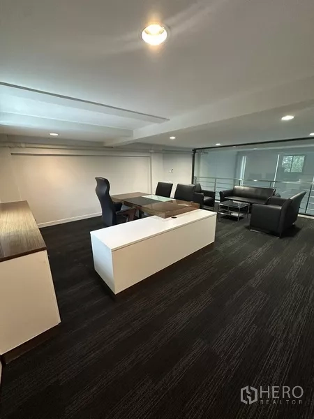 สำนักงานที่บ้าน ให้เช่า - ชั้นลอยห้องผู้บริหาร โต๊ะทำงานและชุดโซฟาบนพรมสีเข้ม