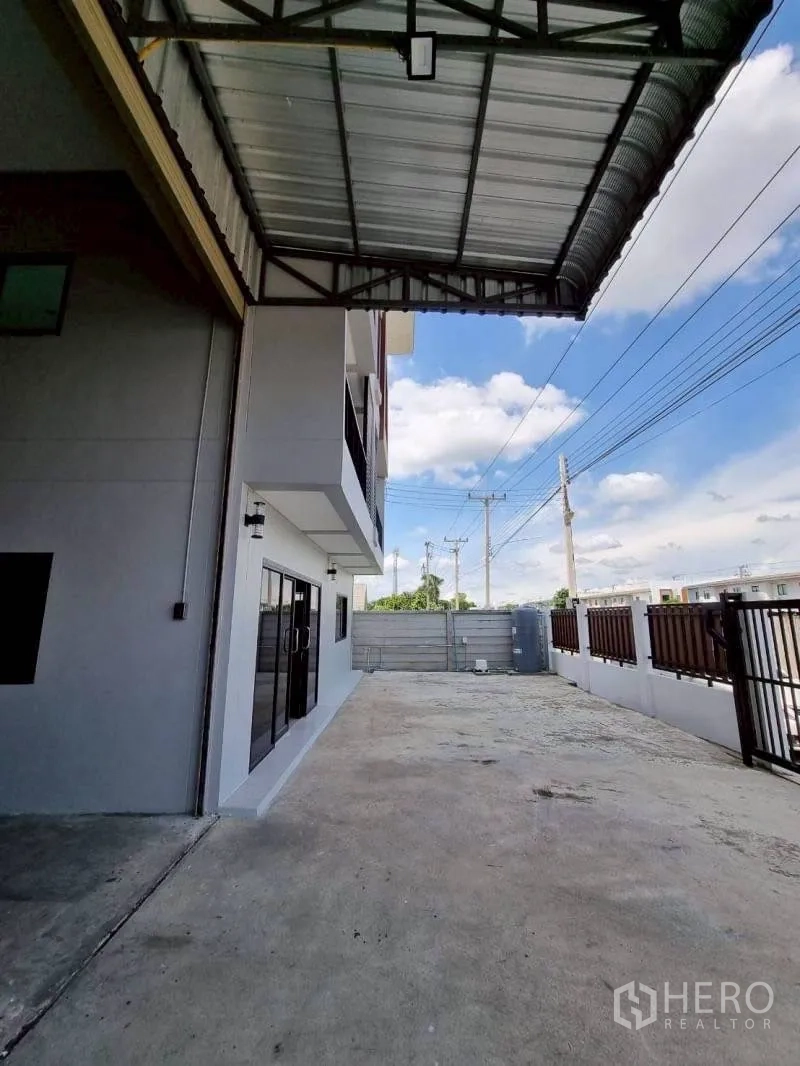 Warehouse for rent in Lam Luk Ka, Pathum Thani - Covered loading area and wide concrete yard beside the building.