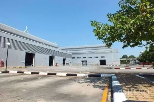 โรงงาน ขายในRayong - ลานกลับรถสำหรับรถบรรทุกขนาดใหญ่ ระหว่างโกดังสีเทาสองหลัง พร้อมช่องโหลดสินค้าและไหล่ทางที่ตีเส้น