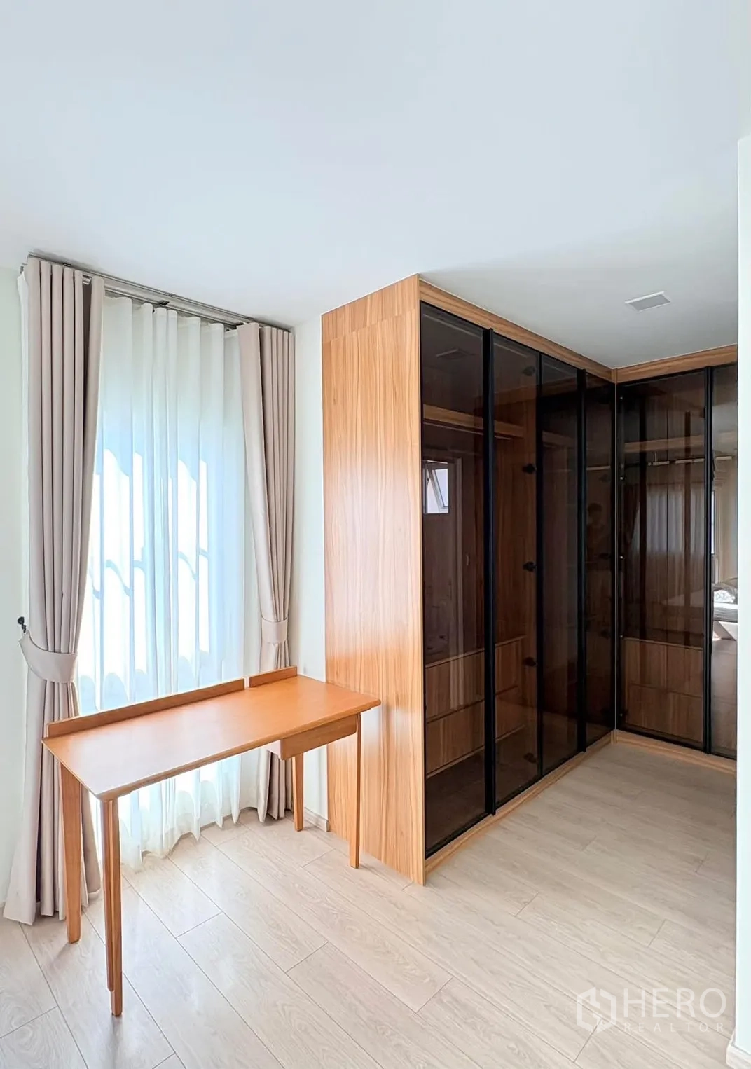 บ้าน for rent in Bang Phli, Samut Prakan - มุมแต่งตัวสว่างพร้อมตู้เสื้อผ้าบานกระจกเข้ามุม โต๊ะไม้ และผ้าม่าน