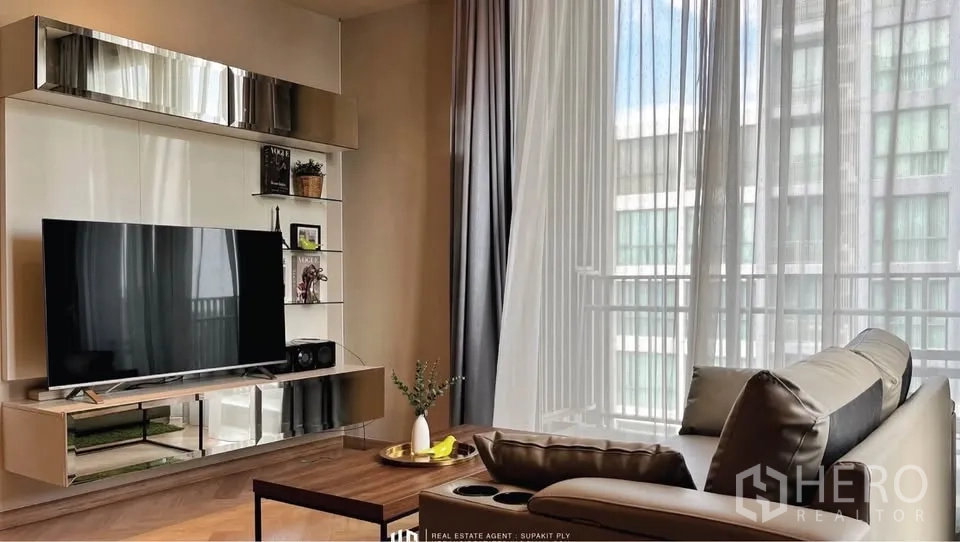 Condominium for rent in Watthana, Bangkok - TV wall with floating shelves opposite a sofa, sheer curtains and natural light.