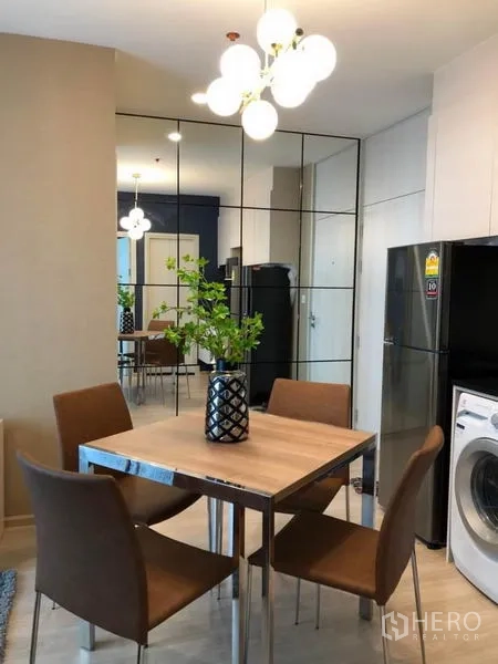 Condominium for rent or sale in Huai Khwang, Bangkok - Dining table for four beside a mirrored feature wall, with refrigerator and washing machine in the corner.