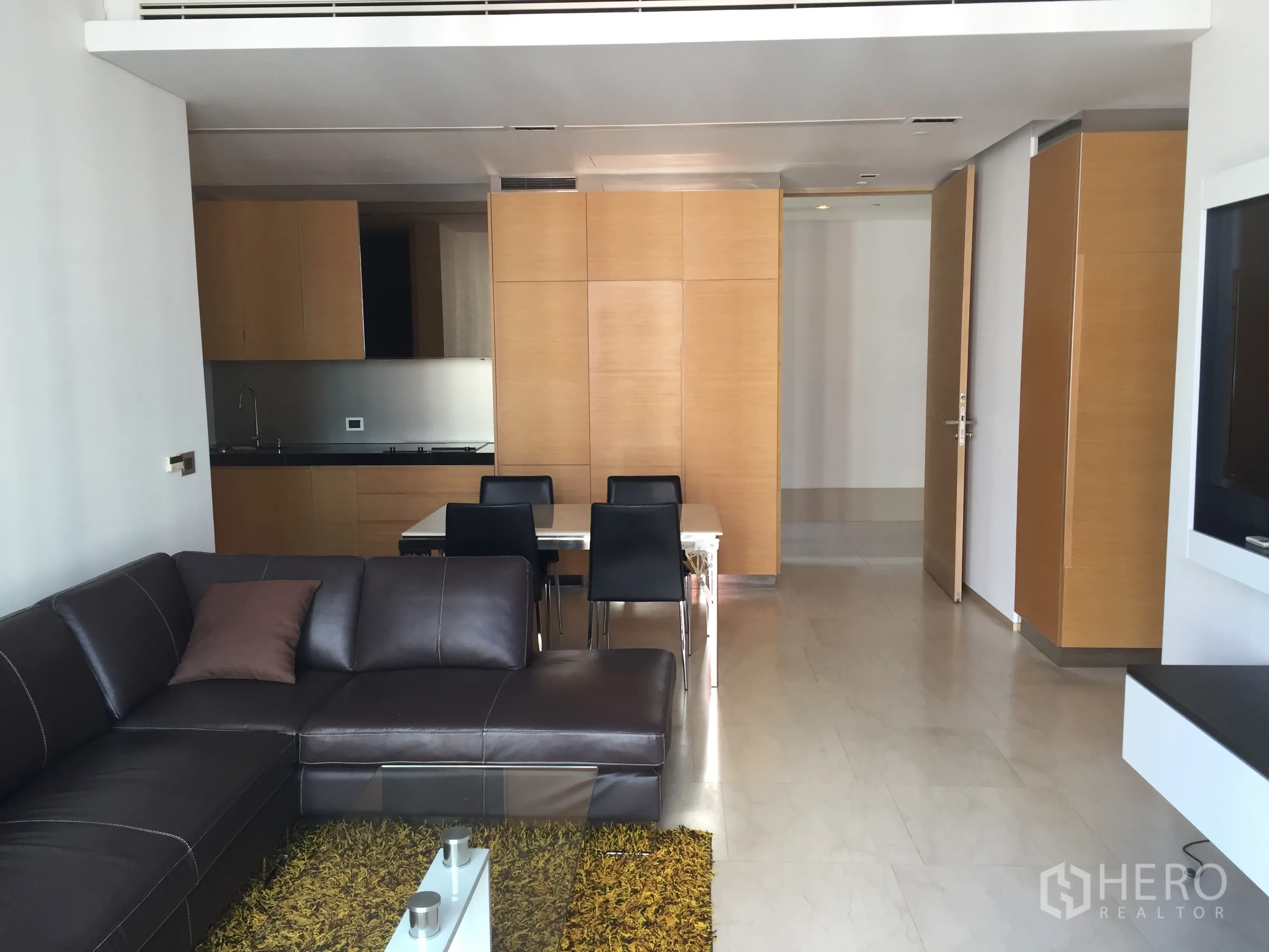 Condominium for rent or sale in Bang Rak, Bangkok - Open-plan living room with leather sectional, dining table and wood kitchen cabinetry.