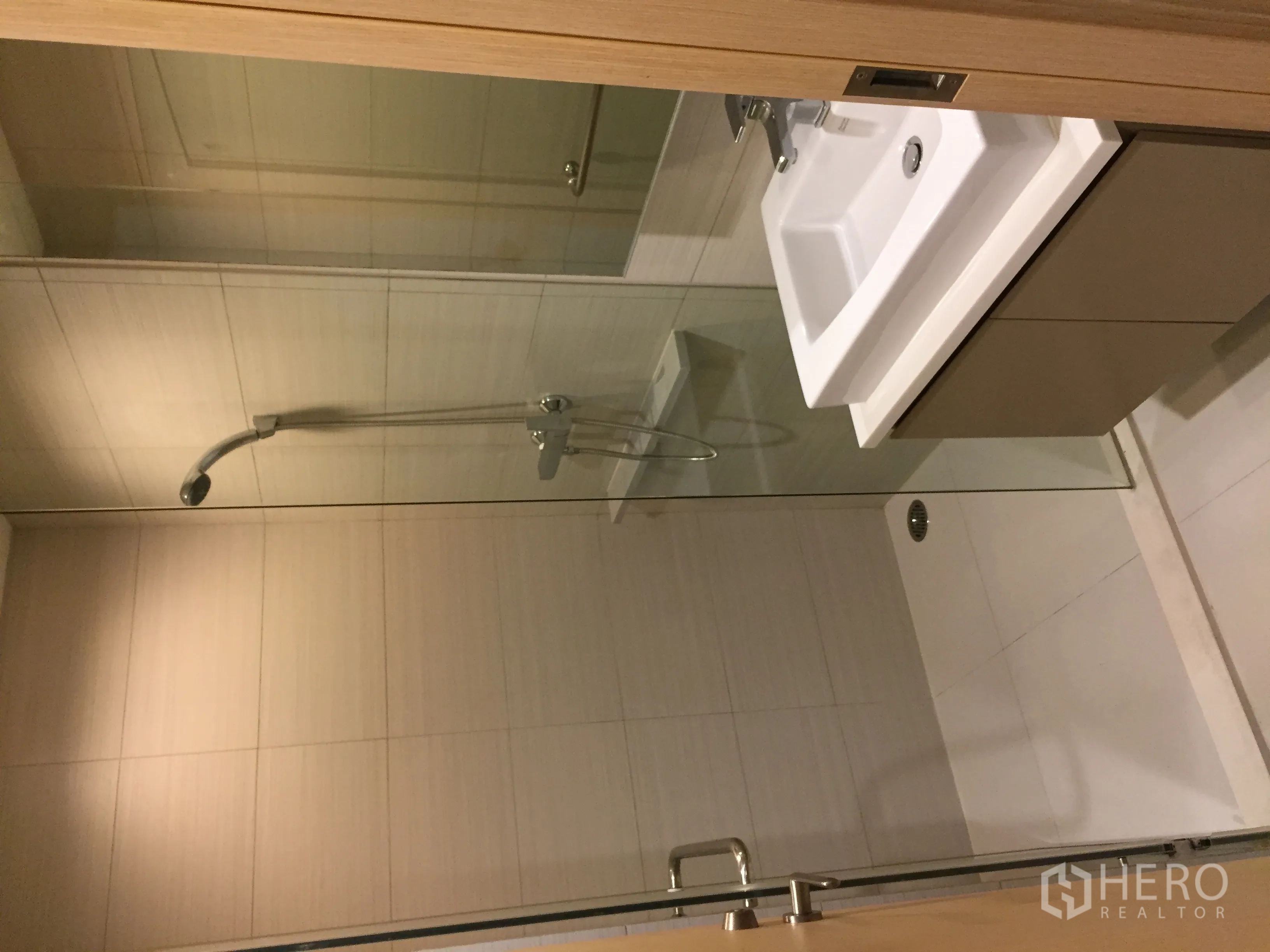 Condominium for rent in Khlong Toei, Bangkok - Contemporary bathroom with glass-enclosed shower and wall-mounted vanity in neutral tiles.