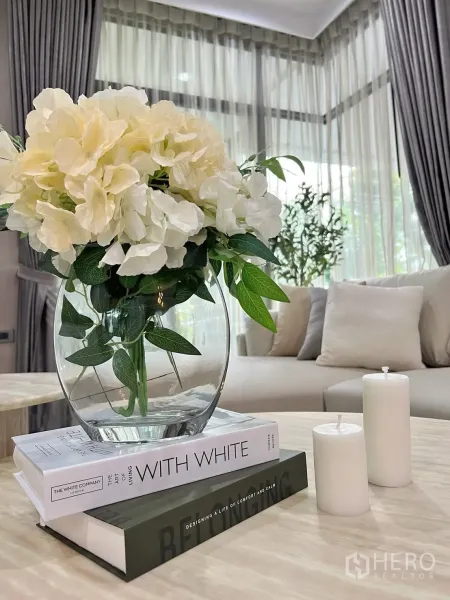 Detached House for rent in Prawet, Bangkok - Coffee table decor with a glass vase of flowers, books, and candles in a light-filled living room.