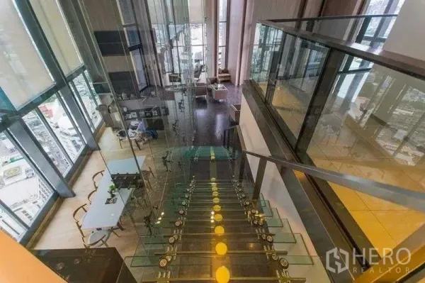 Condominium for rent in Khlong Toei, Bangkok - Sky lounge with a glass staircase, double-height windows and sweeping city skyline views.