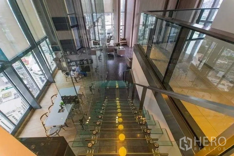 Condominium for rent in Khlong Toei, Bangkok - Sky lounge with a glass staircase, double-height windows and sweeping city skyline views.