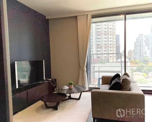 公寓 出租在Watthana, Bangkok - 客厅采光明亮，沙发与电视墙，落地窗连接阳台，可观城市景观。