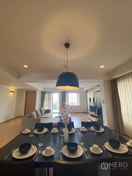 Apartment for rent in Watthana, Bangkok - View from the dining table to the living room with sofa, TV console and large curtained windows.