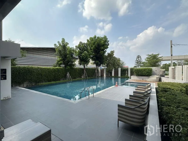 Detached House for sale in Sai Mai, Bangkok - Residents’ swimming pool with sun deck chairs and hedges.