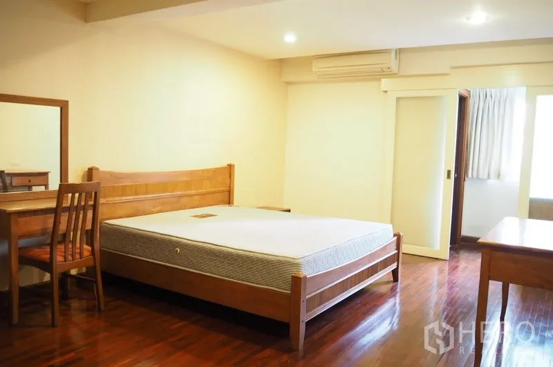คอนโด ให้เช่าในPathum Wan, Bangkok - ห้องนอนกว้างเตียงไม้ โต๊ะทำงาน และประตูสู่ห้องน้ำในตัว