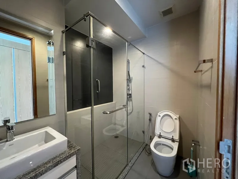 Condominium for rent in Khlong Toei, Bangkok - Contemporary bathroom with glass-enclosed shower and sleek fixtures.