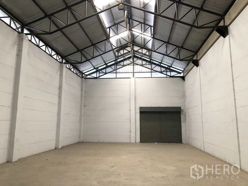 货栈 出租在Lat Lum Kaeo, Pathum Thani - 空旷仓库内部，高挑钢架人字形屋顶与大型卷帘门。