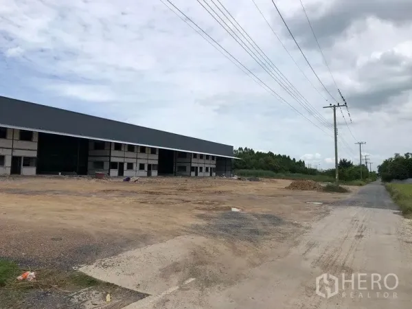 货栈 出租在Khlong Luang, Pathum Thani - 通往园区的道路与宽阔场地，旁为长排仓库及电线杆