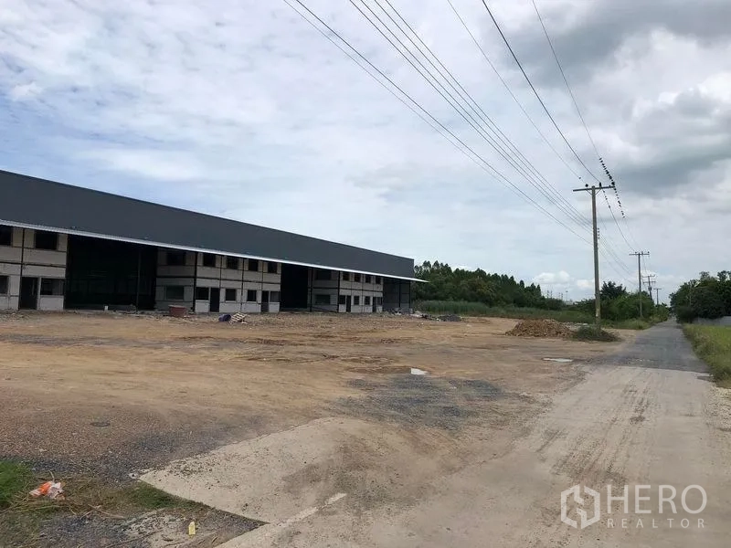 货栈 出租在Khlong Luang, Pathum Thani - 通往园区的道路与宽阔场地，旁为长排仓库及电线杆
