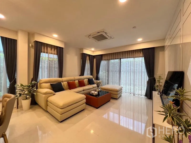 Detached House for rent or sale in Saphan Sung, Bangkok - Bright living room with L-shaped sectional sofa and floor-to-ceiling windows.