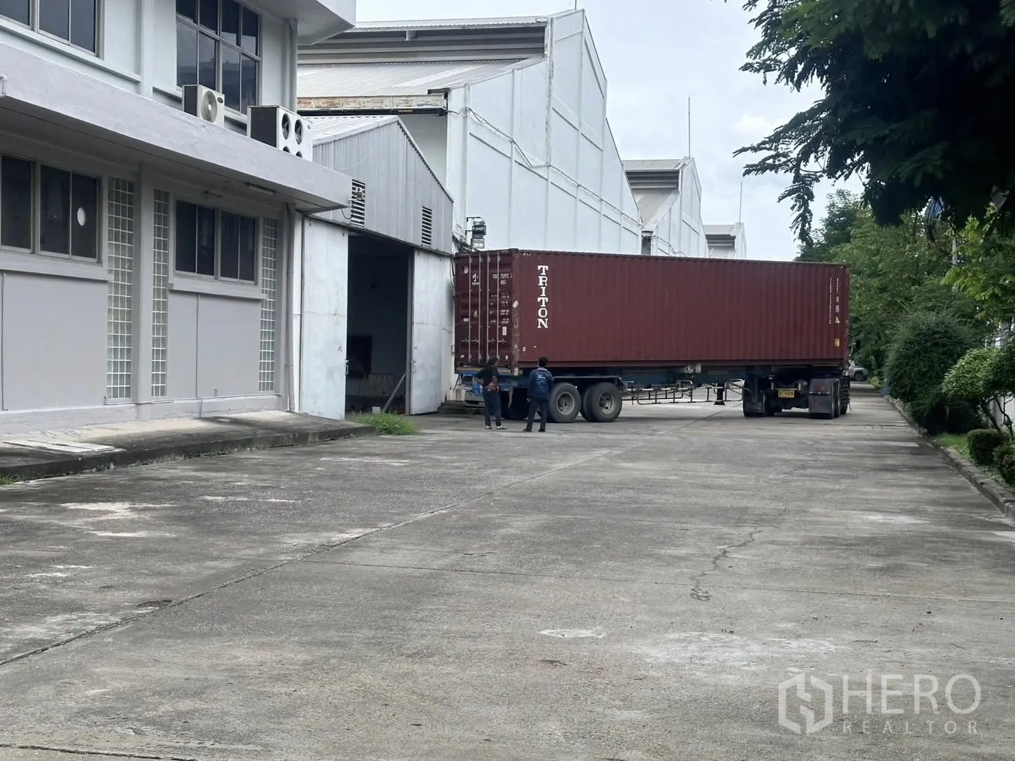 Warehouse for rent in Mueang Samut Prakan, Samut Prakan - Wide concrete driveway beside warehouse blocks and office building, suitable for container truck access.
