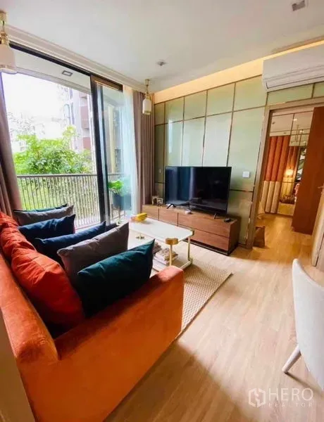 คอนโด ให้เช่าในWatthana, Bangkok - ห้องนั่งเล่นสว่าง โซฟาสีส้ม ชั้นวางทีวี และระเบียงวิวต้นไม้ในคอนโดสไตล์โมเดิร์น
