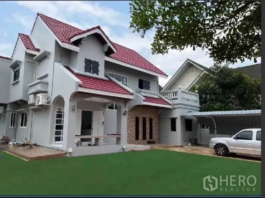 Detached House for rent in Samut Prakan - Front view of the house with carport, driveway, and landscaped yard.