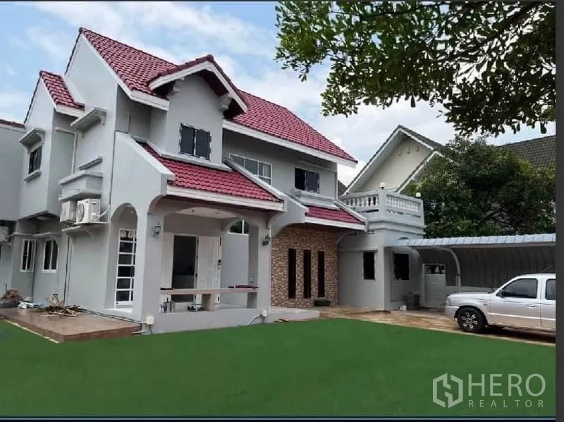 Detached House for rent in Samut Prakan - Front view of the house with carport, driveway, and landscaped yard.