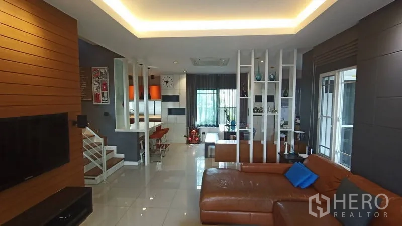 บ้าน ขายในPrawet, Bangkok - ห้องนั่งเล่นกว้าง โซฟาหนังตัวแอล ฉากกั้นโปร่งเชื่อมสู่รับประทานอาหารและบันได