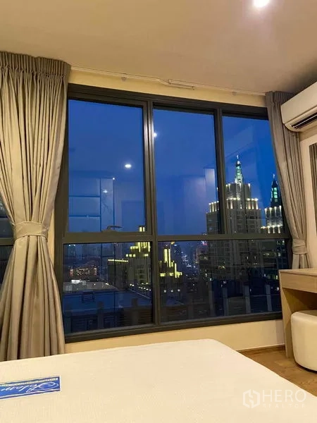 公寓 出租或出售在Ratchathewi, Bangkok - 卧室内可观赏傍晚灯火辉煌的曼谷天际线。