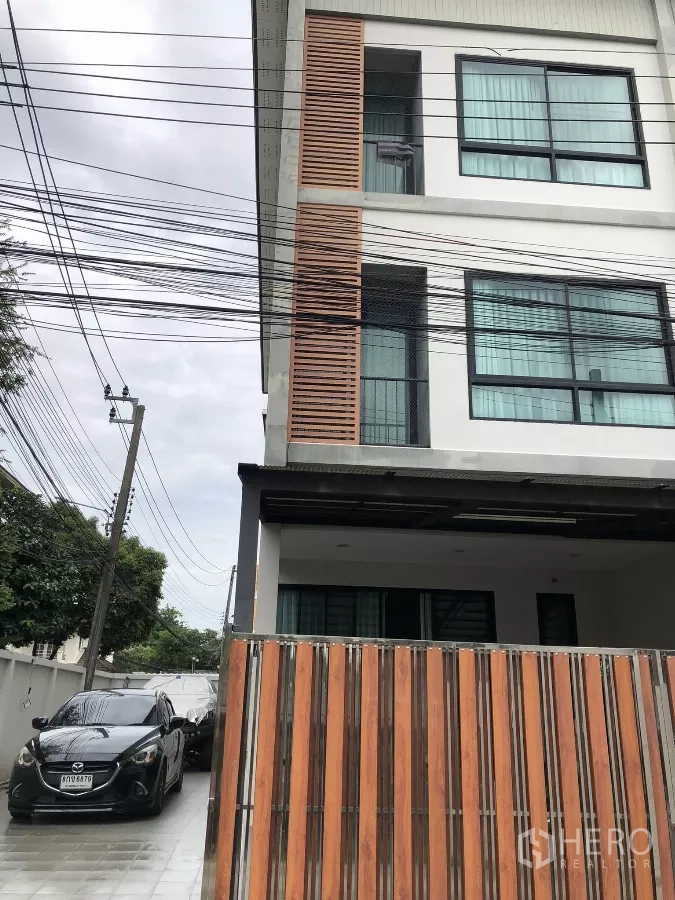 Townhouse for sale in Phra Khanong, Bangkok - Modern three-storey townhouse facade in Phra Khanong with wood slats, large windows and a gated driveway.