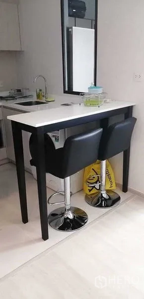 公寓 出租或出售在Pathum Wan, Bangkok - 纤细吧台配两把黑色吧椅，临近紧凑小厨房。