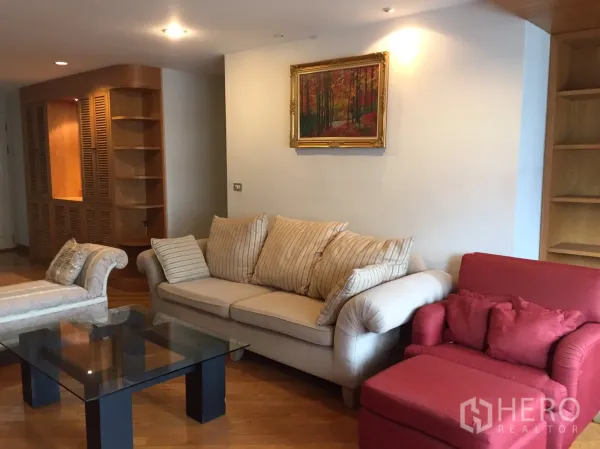 Condominium for rent in Pathum Wan, Bangkok - Cozy living room with cream sofa, red armchair, glass coffee table and built-in wooden shelving on hardwood floors.