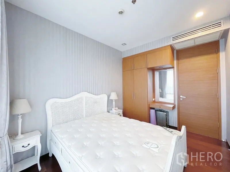Condominium for sale in Khlong Toei, Bangkok - Light bedroom with white bed, bedside tables and a built-in wardrobe with dressing nook.