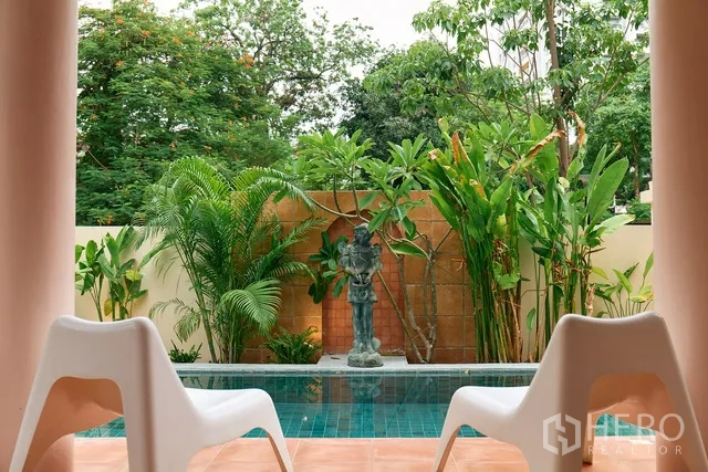 Detached House for rent in Watthana, Bangkok - Poolside terrace with two lounge chairs and a water feature amid lush plants.