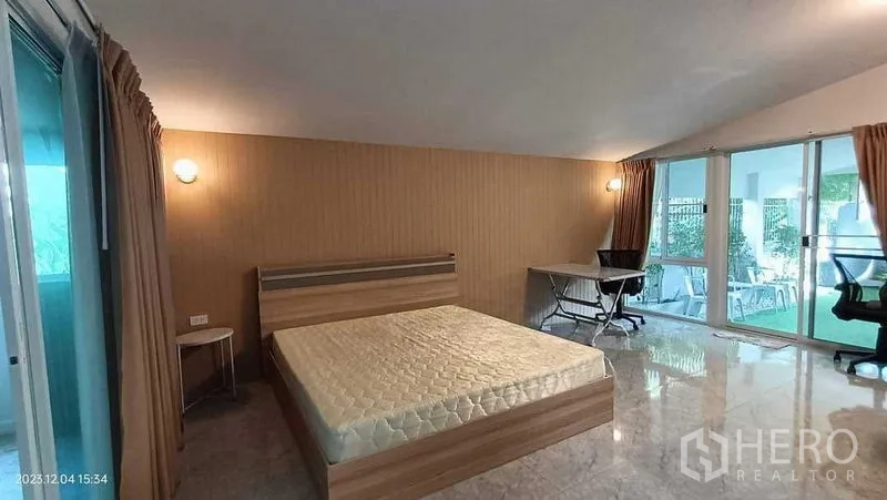 Detached House for rent in Lam Luk Ka, Pathum Thani - Large bedroom with wood bed, desk and sliding glass doors to patio.