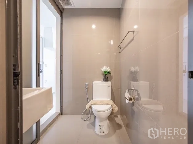 Condominium for sale in Khlong Toei, Bangkok - Separate toilet area with towel rack and sliding door in neutral tiles.