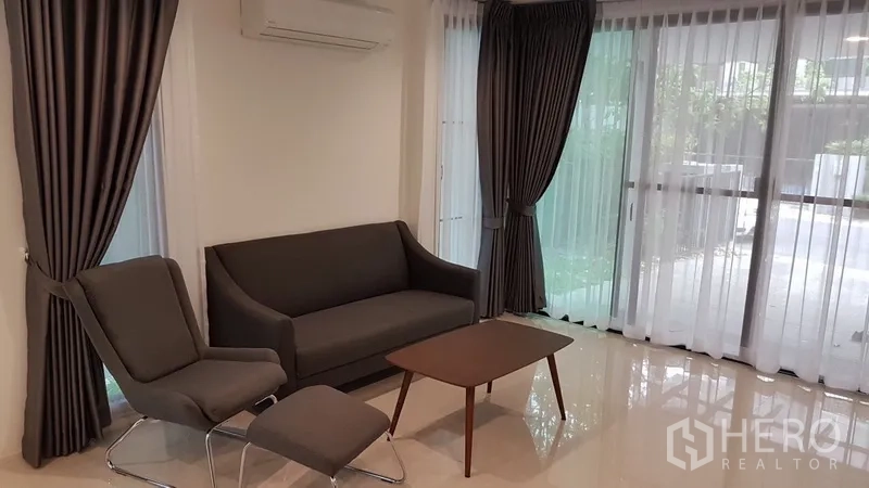 บ้าน ให้เช่าในPrawet, Bangkok - ห้องนั่งเล่นสว่าง โซฟาสีเทา ผ้าม่านสูงจรดเพดาน และพื้นกระเบื้องเงา.