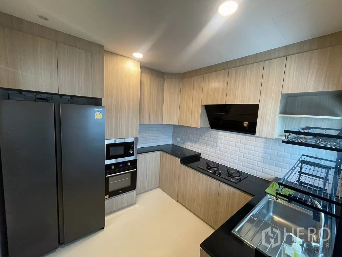 独立式住宅 出租在Bang Phli, Samut Prakan - 全配套厨房，木饰柜体、黑色台面与内嵌电器。