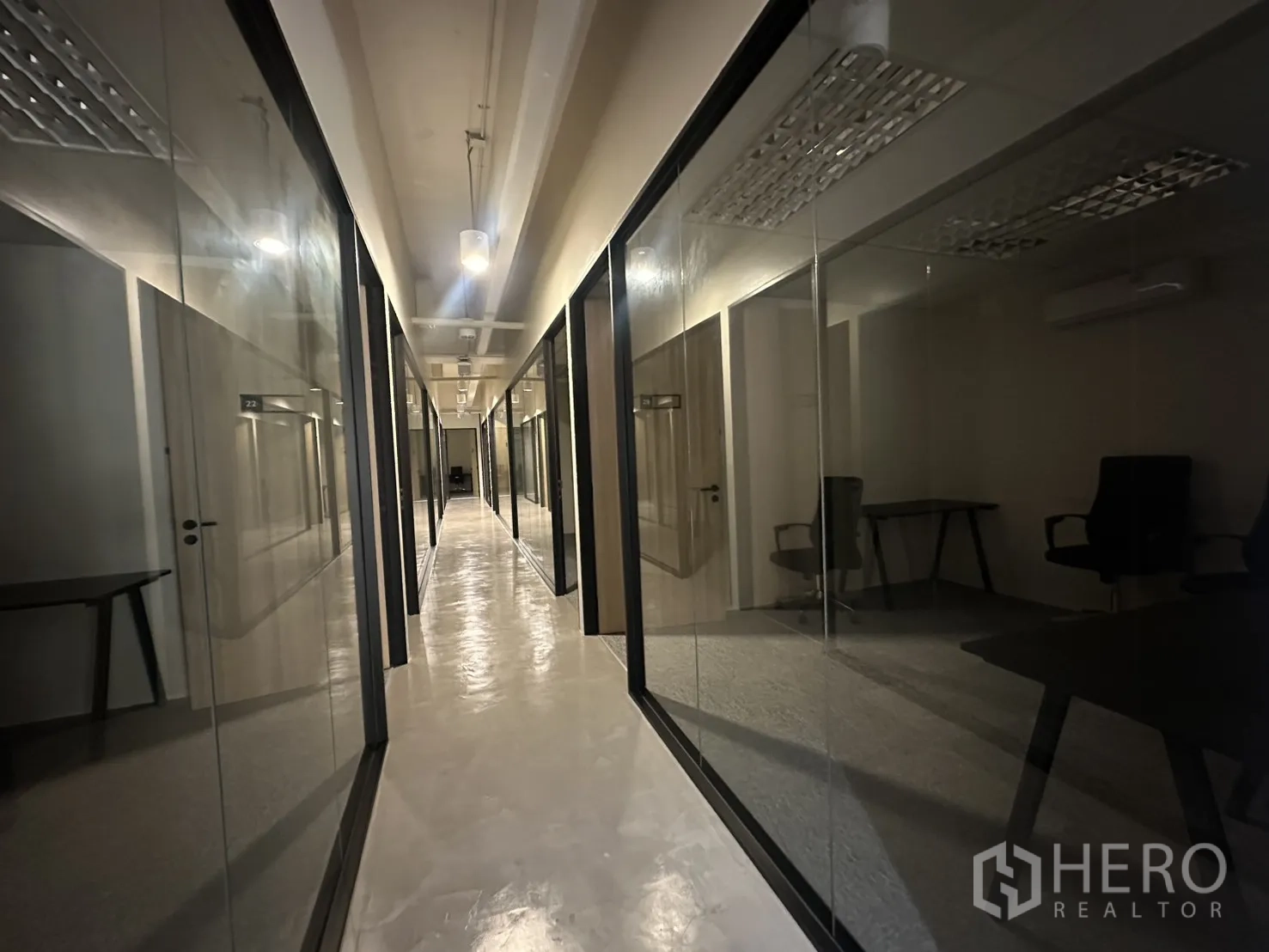Office Space for rent in Bang Rak, Bangkok - Dim corridor lined with glass office fronts and industrial-style ceiling lighting.