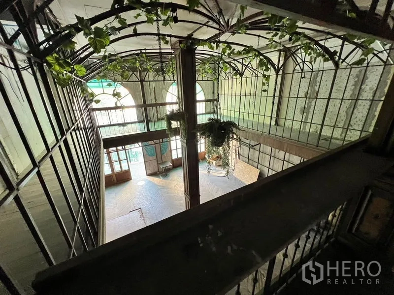 Shophouse for rent in Watthana, Bangkok - Overhead view of an atrium with hanging plants, arched windows, and mezzanine walkways.
