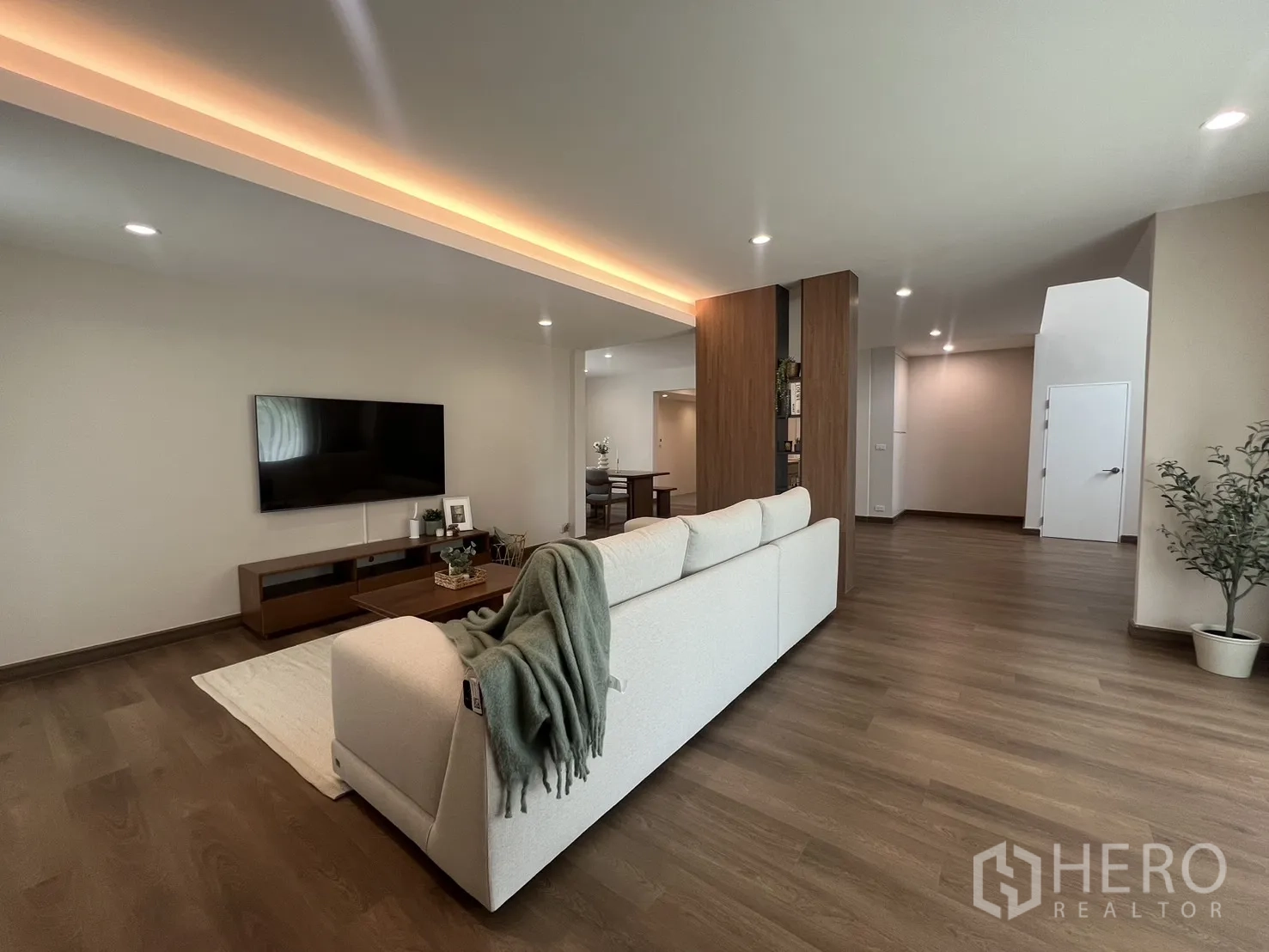 Detached House for rent in Mueang Samut Prakan, Samut Prakan - Bright living room with L-shaped sofa, TV wall and wooden floors.