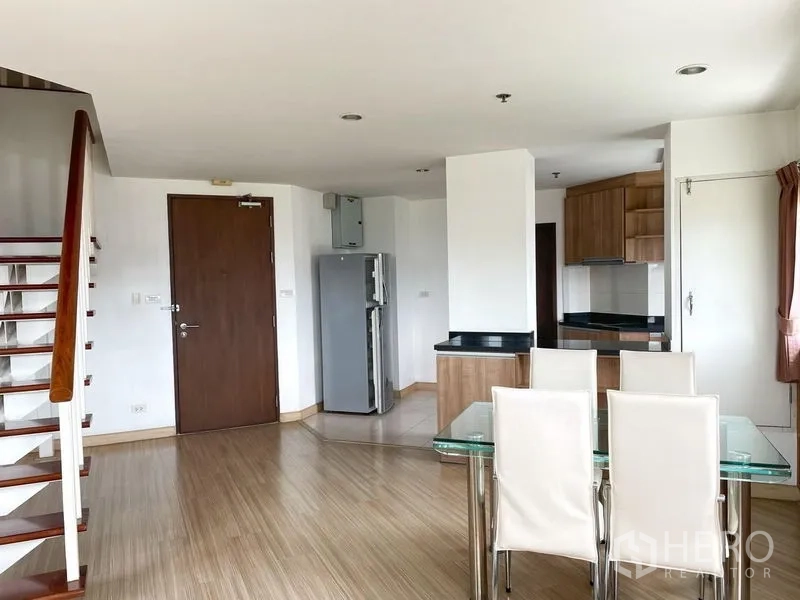 Condominium for rent in Khlong Toei, Bangkok - Dining area with glass-top table and white chairs next to the open kitchen and entry door.