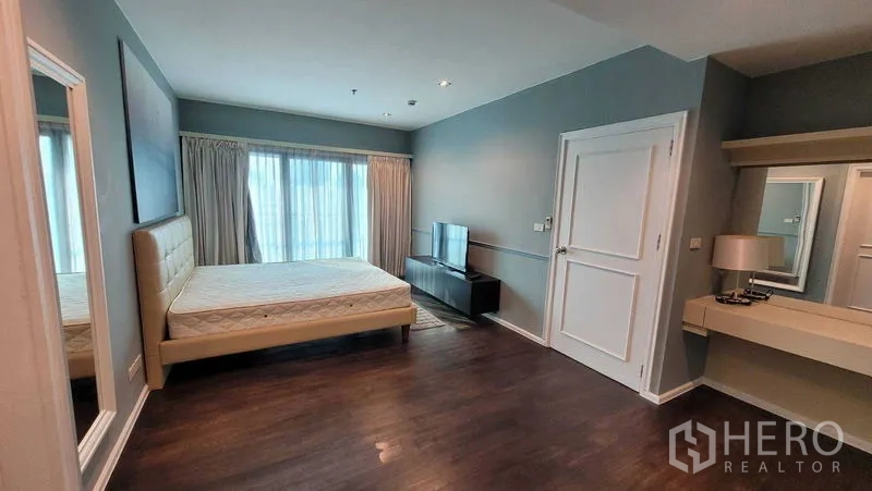 Condominium for rent in Khlong Toei, Bangkok - Master bedroom with king bed, large windows, TV console and vanity in soft blue tones.
