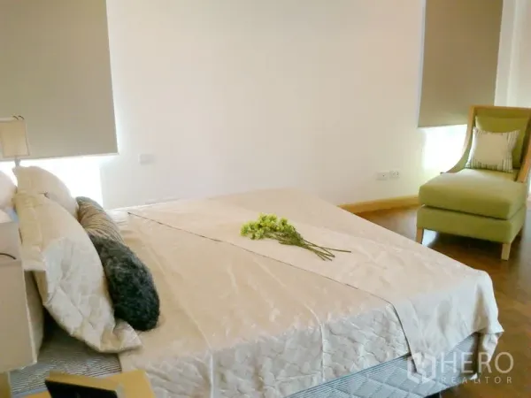 Condominium for rent in Khlong Toei, Bangkok - Cozy bedroom with upholstered chair, neutral bedding and window blinds.