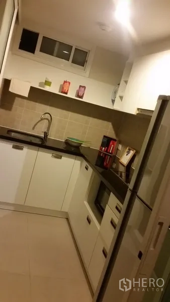 Condominium for rent in Khlong San, Bangkok - Modern L-shaped kitchen with white cabinetry, granite countertops and a full-size refrigerator.