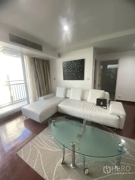 Condominium for rent in Watthana, Bangkok - Bright living room with white L-shaped sofa, glass coffee table, balcony doors and hardwood floors.